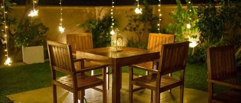 An outdoor dining area with a wooden table and chairs, string lights, and a lantern.