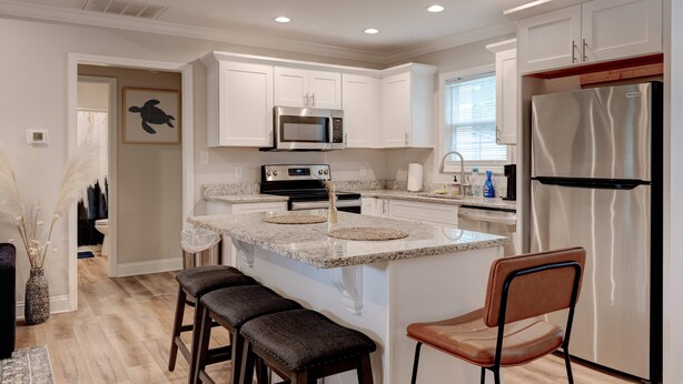 Una cocina moderna con armarios blancos, un refrigerador de acero inoxidable, un microondas y una isla central con taburetes de bar.
