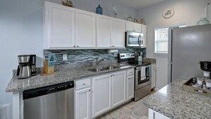 Una cocina moderna con armarios blancos, encimeras de granito, electrodomésticos de acero inoxidable y salpicadero de azulejos azules.