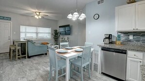 Una cocina compacta con armarios blancos, lavavajillas y un comedor con mesa y sillas.
