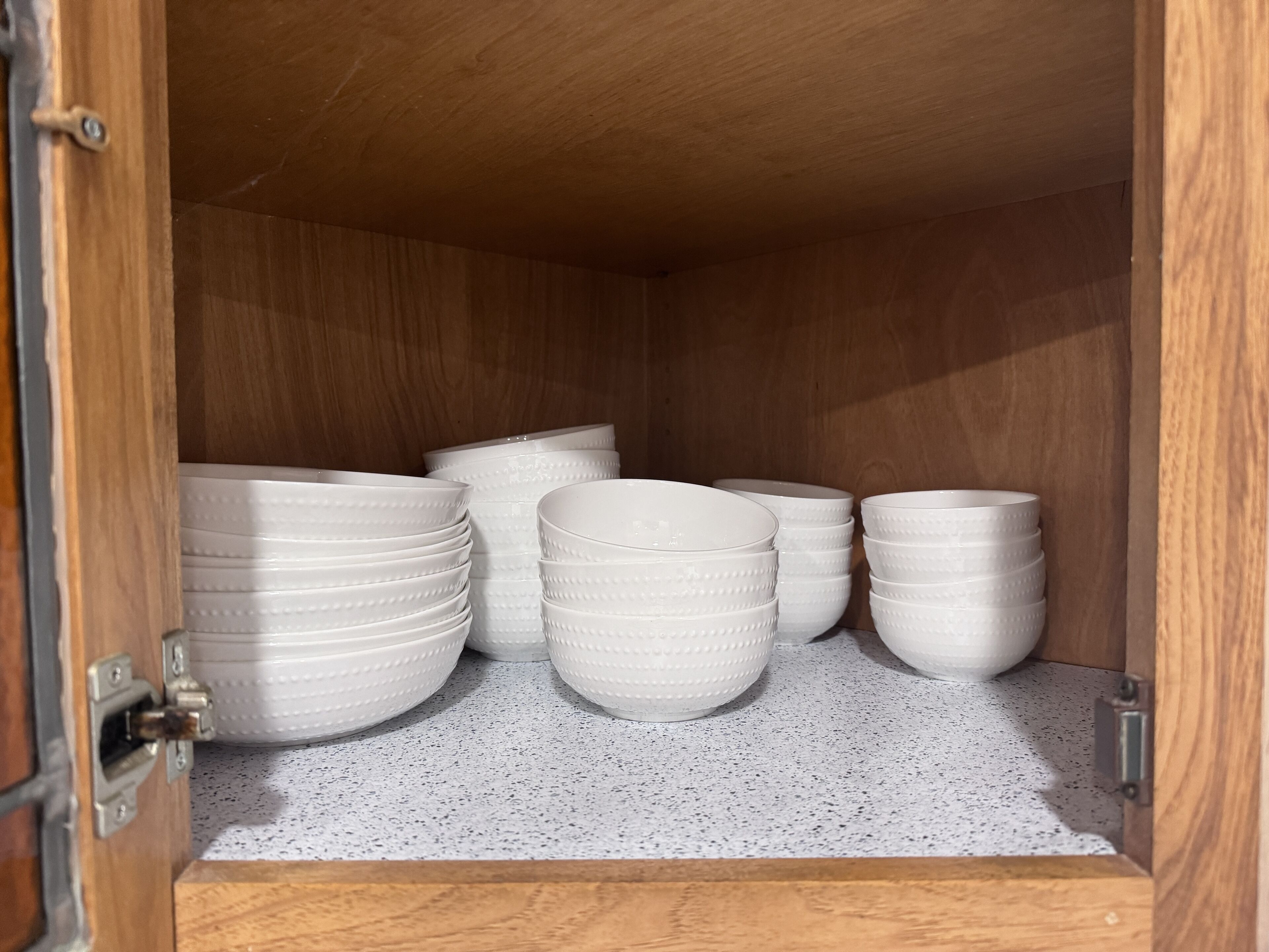 Un mueble de madera con cuencos de cerámica blanca apilados en su interior.