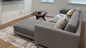 Una sala de estar con un sofá gris, una mesa de centro y un televisor de pantalla plana montado en la pared.