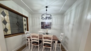 Un comedor con una mesa de madera y sillas blancas, un tapete estampado y un ventilador de techo.