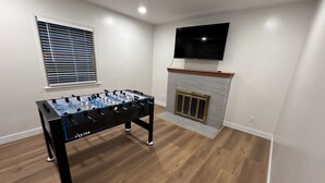 Una habitación con mesa de fútbol, chimenea y televisor montado.