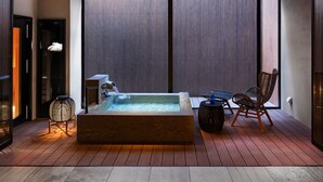 Ein moderner Außenbereich mit Whirlpool, einer Holzterrasse, einer Sitzecke und Blick durch große Schiebetüren.