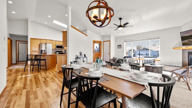 A modern kitchen with wooden cabinets, a dining area with a wooden table and chairs, and a large window offering a view of the outdoors. - Modern Lodge with a Jacuzzi Tub (Bend)