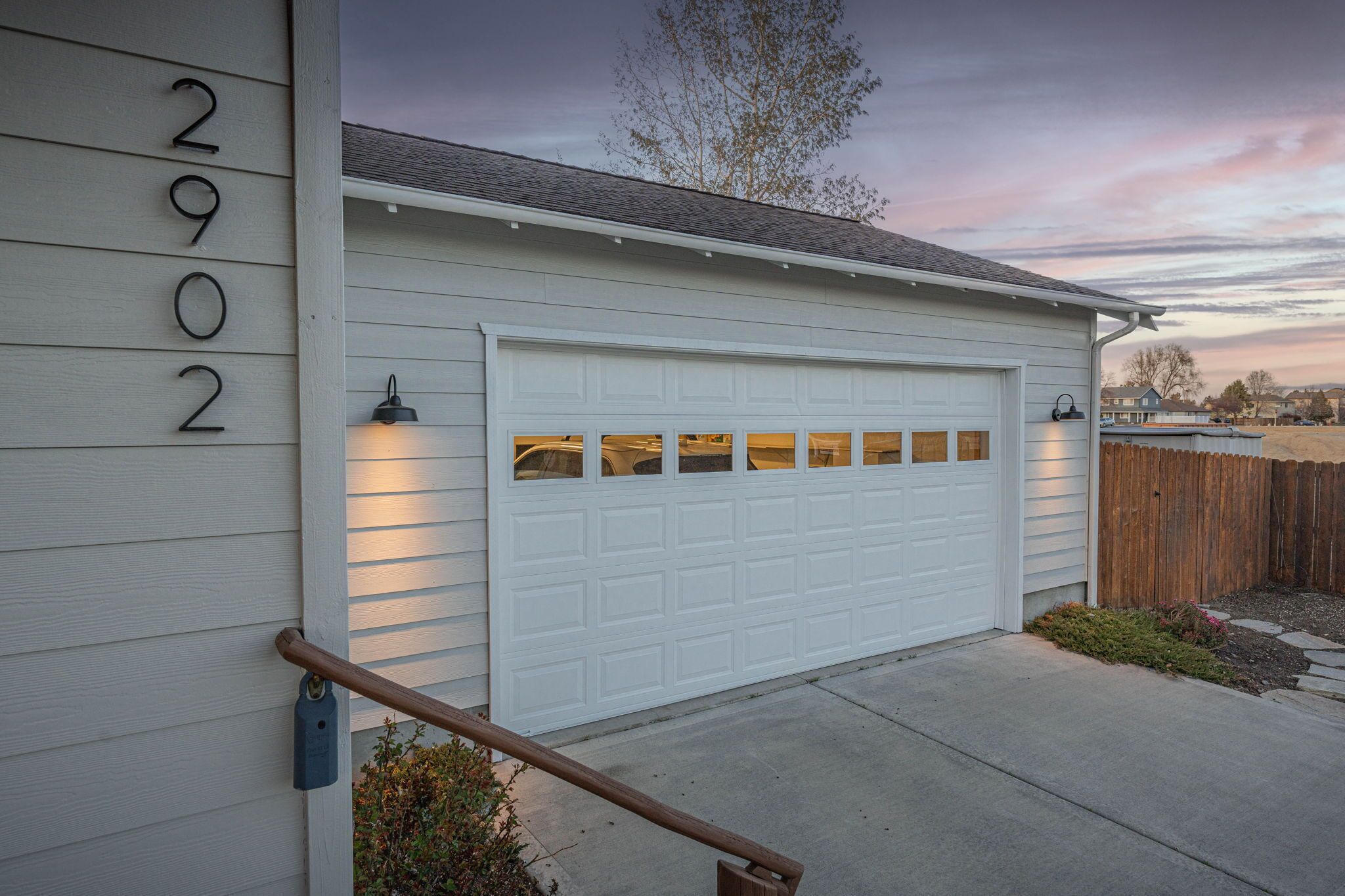A residential garage with a white door, a metal number '2902' sign, and a wooden handrail.
