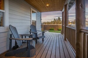 A wooden deck with Adirondack chairs and a table, overlooking a fenced yard with trees. - Modern Lodge with a Jacuzzi Tub (Bend)