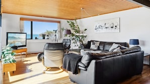 A modern living room with a large leather sofa, a television, and a view of the outdoors.