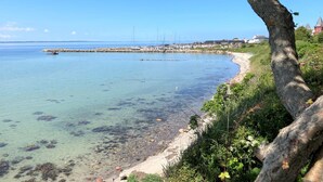A coastal view with a clear sky, a sandy beach, and a rocky outcrop with boats.