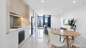 A modern kitchen with a dining area, a large window with a city view, and a flat-screen TV on the wall. - Luxe Oceanfront 1-Bed High Rise with Pool & Gym (Surfers Paradise)