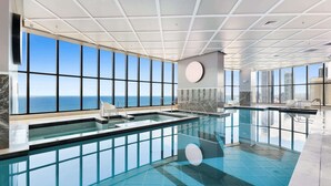 A large indoor swimming pool with a view of the ocean through large windows. - Luxe Oceanfront 1-Bed High Rise with Pool & Gym (Surfers Paradise)