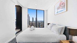 A modern hotel room with a large bed, a city view, and a framed picture on the wall. - Luxe Oceanfront 1-Bed High Rise with Pool & Gym (Surfers Paradise)