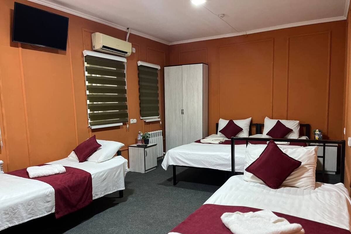 A hotel room with three beds, a TV, an air conditioning unit, and a radiator.