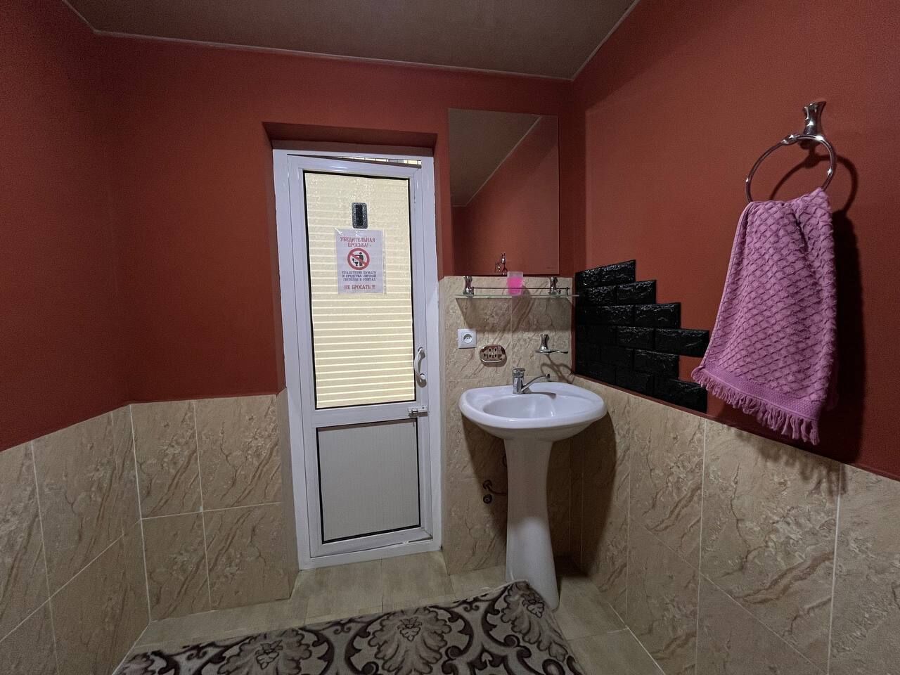 A bathroom with a white sink, a towel rack with a pink towel, and a door with a sign.