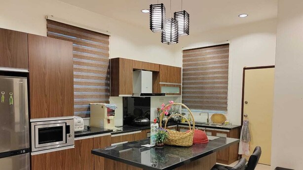 A modern kitchen with wooden cabinets, a stainless steel refrigerator, a microwave, and a built-in oven. There is a black countertop island with a basket and a red kettle. - Nice semi D house at Tangkak (Tangkak)