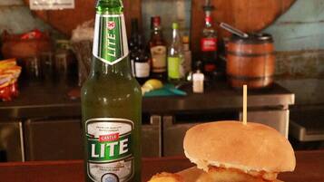 Eine Mahlzeit mit einem Burger, Zwiebelringen und einem Salat, sowie eine Flasche Castle Lite Bier auf einem Tisch.