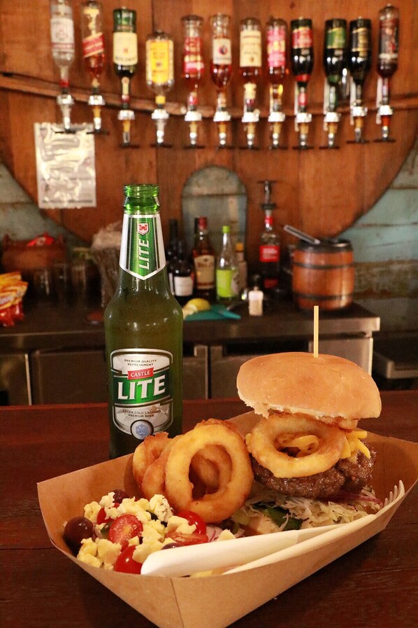 Una comida con una hamburguesa, aros de cebolla, una ensalada y una botella de Castle Lite sobre una mesa.