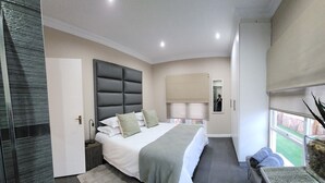 A modern bedroom with a large bed, a bedside table, a nightstand, a mirror, and a window with a view. - Bon Game Reserve (Albertinia)