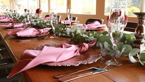 A long dining table set with pink napkins, clear wine glasses, and silverware, surrounded by greenery and a view of the outdoors. - Bon Game Reserve (Albertinia)