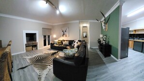 A spacious living area with a fireplace, a sofa set, a zebra rug, and a kitchen area with a refrigerator. - Bon Game Reserve (Albertinia)