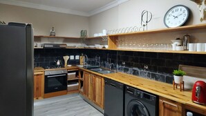 A modern kitchen with wooden cabinets, a dishwasher, a washing machine, a sink, and a clock on the wall. - Bon Game Reserve (Albertinia)