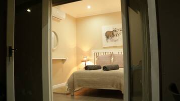 Un dormitorio con cama, almohadas, una lámpara de noche y aire acondicionado de pared.