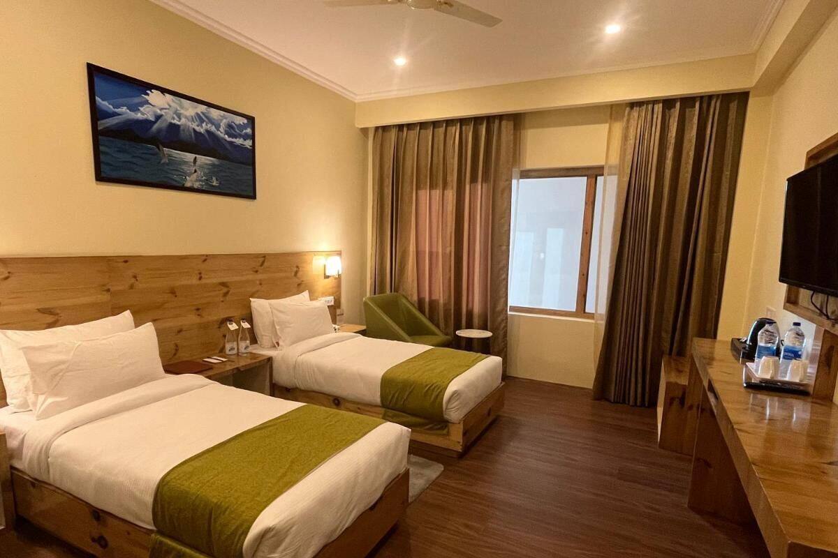 Habitación de hotel con dos camas, un escritorio, una silla, un televisor y una ventana con cortinas.