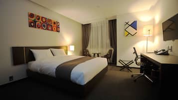 Habitación de hotel con una cama grande, un escritorio con silla, una lámpara y un cuadro en la pared.