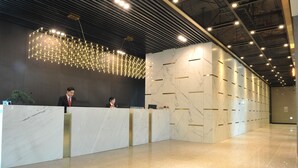A reception area with a marble reception desk, a modern chandelier, and a marble wall with a geometric pattern. - Yongin Central CO'OP Hotel (Yongin)