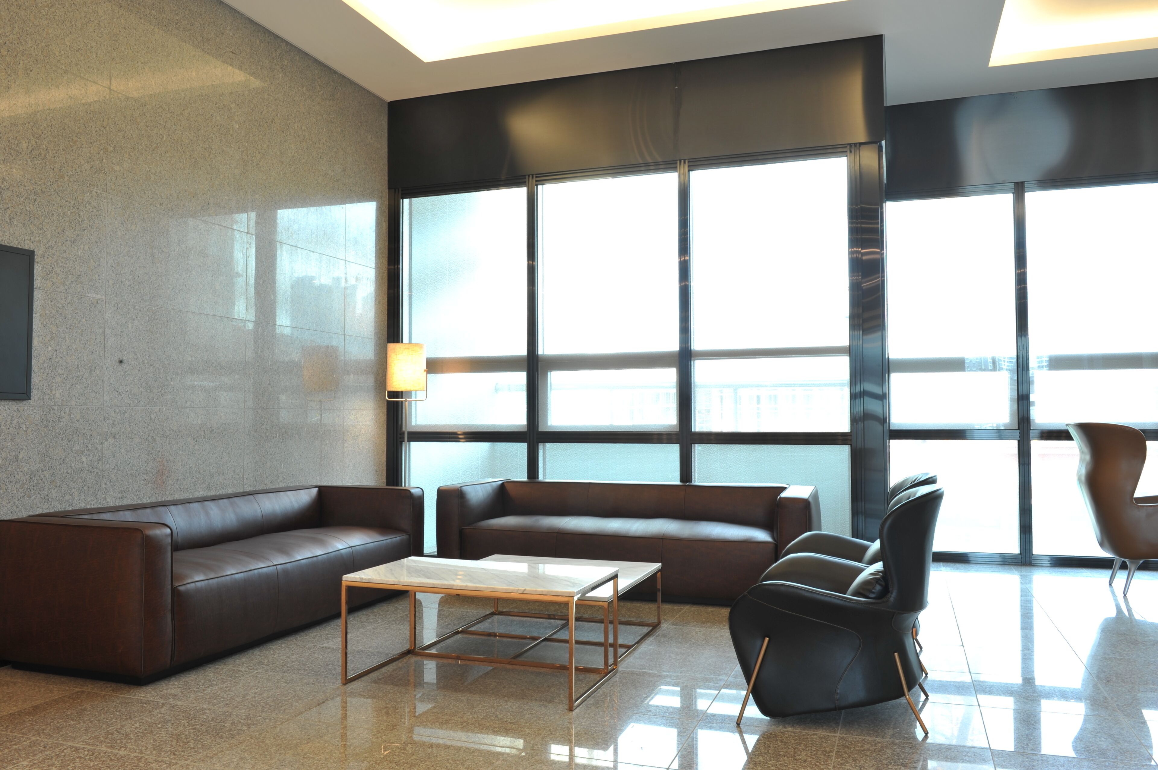 A modern lobby with two sofas, a coffee table, and a chair. Large windows provide natural light.