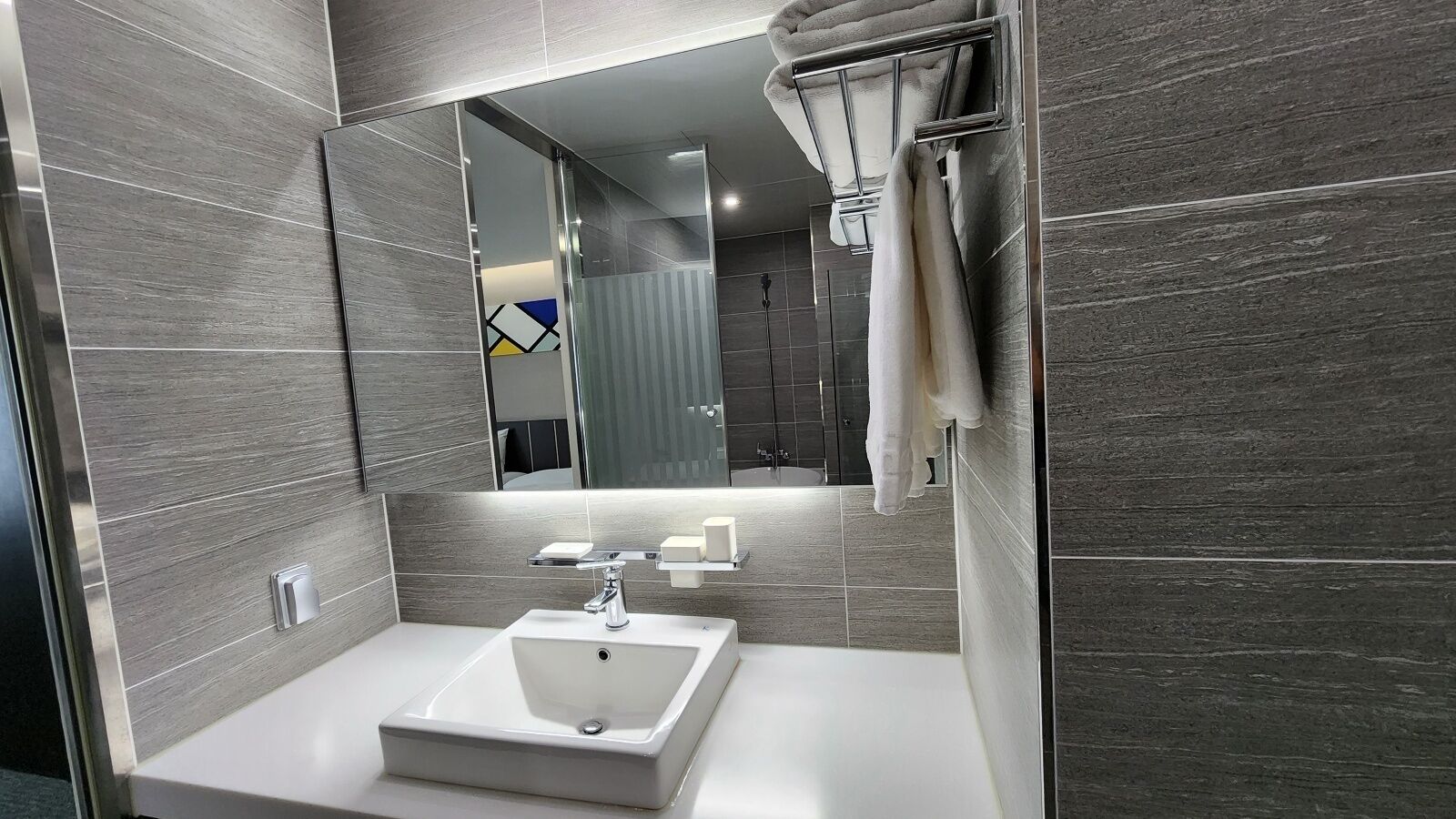 Ein modernes Badezimmer mit einem großen Spiegel, einem weißen Waschbecken und einem Handtuchhalter.