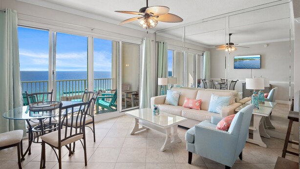 Een ruime woonkamer met een balkon met uitzicht op de oceaan, ingericht met een glazen tafel, stoelen, een bank en een salontafel.