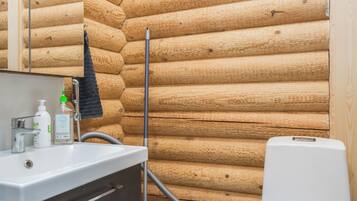 Een badkamer met een wand van houten boomstammen, een wastafel met spiegel en een wit toilet.