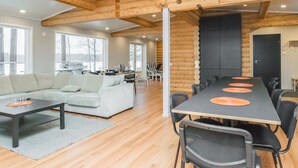 Een ruime woonkamer met een grote bank, een eettafel met stoelen, en een keuken op de achtergrond.
