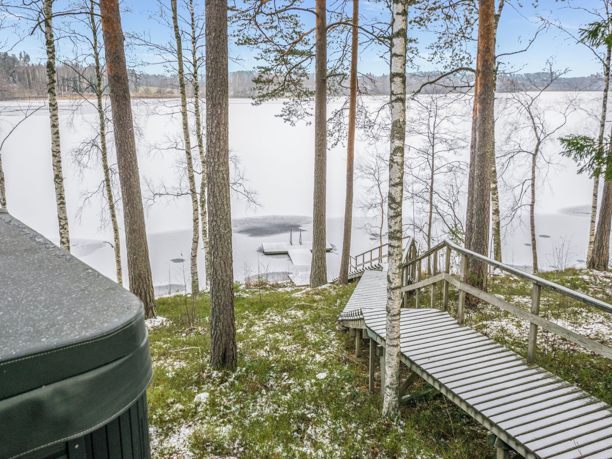 A wooden deck leading to a cabin with a view of a frozen lake surrounded by trees.