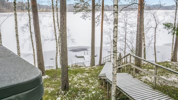 A wooden deck leading to a cabin with a view of a frozen lake surrounded by trees.