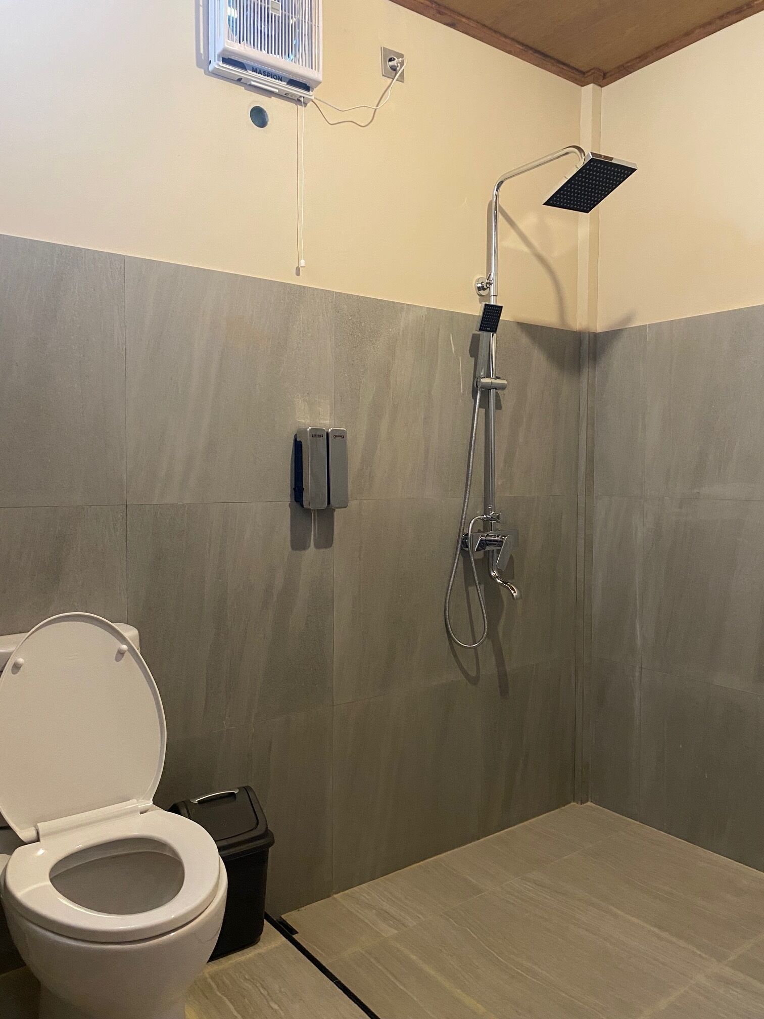 A bathroom with a toilet, a shower, and a wall-mounted air conditioning unit.