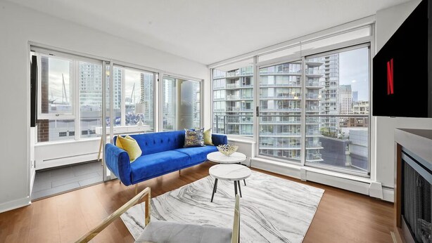 Een moderne woonkamer met een blauwe bank, een klein rond tafeltje en grote ramen met uitzicht op de stad.