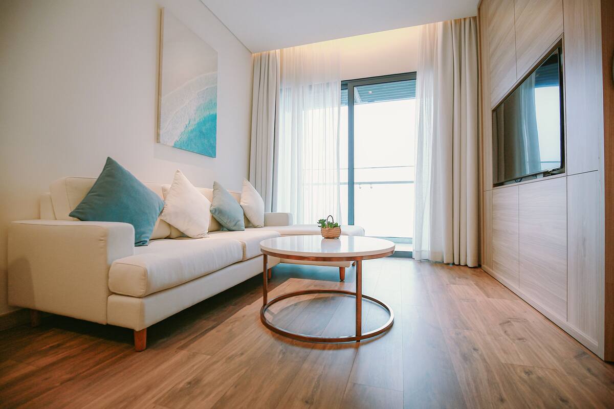 Ein modernes Wohnzimmer mit einem weißen Sofa, einem runden Couchtisch und einem großen Fenster mit Vorhängen.