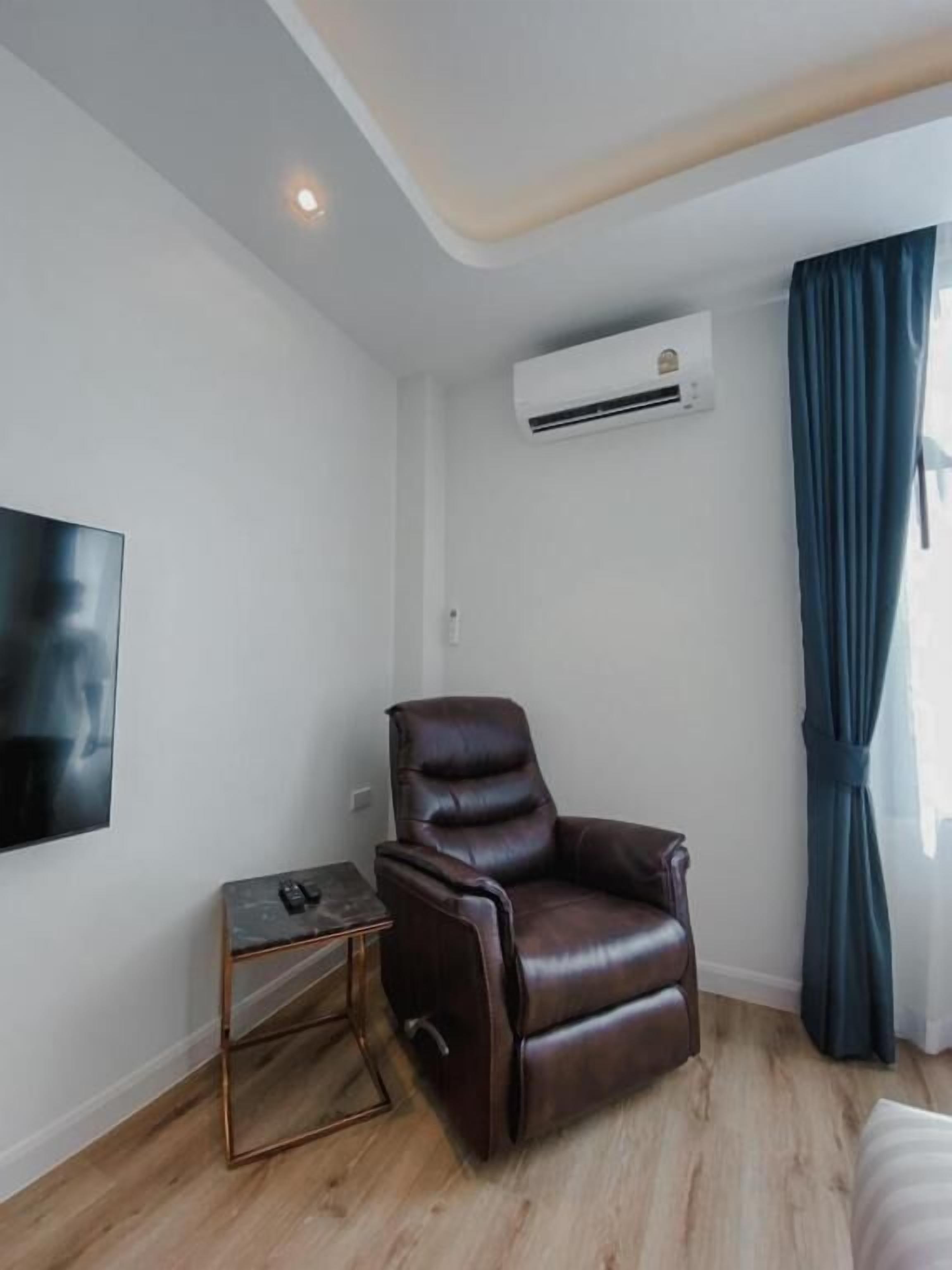Een kamer met een leren relaxfauteuil, een klein bijzettafeltje, een wandgemonteerde flatscreen-tv en een airconditioning.