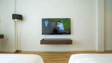 Une chambre d’hôtel équipée d’un téléviseur à écran plat fixé au mur, d’une table de chevet et d’une lampe sur pied.