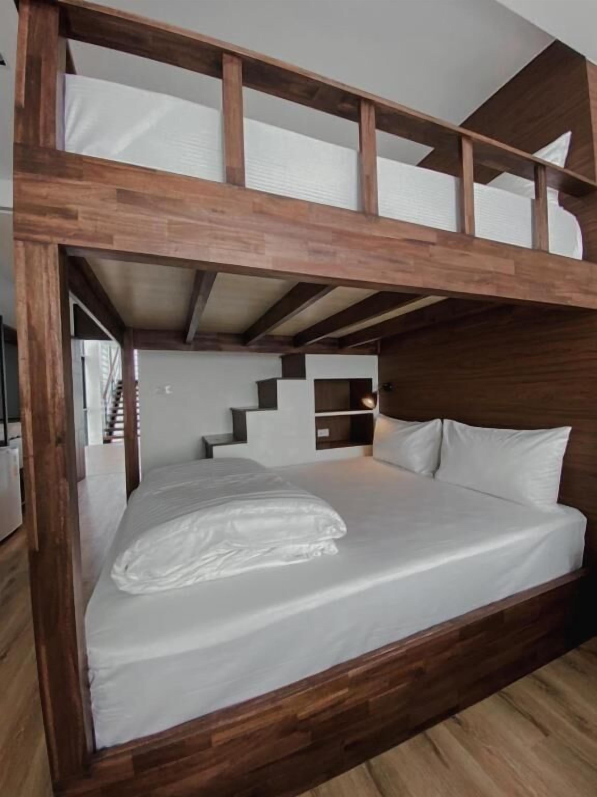 A bunk bed with a wooden frame, white bedding, and a staircase leading to an upper bunk.