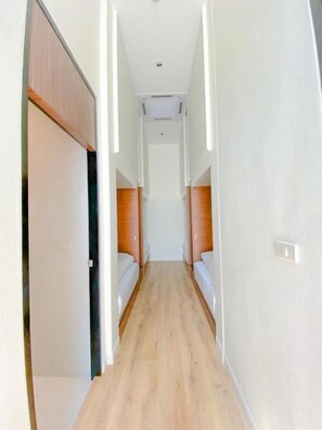A narrow hallway with wooden flooring and white walls, leading to a room with a bed. - Play Poshtel & Cafe (Krabi)