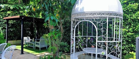 Un jardín con un mirador, mobiliario exterior y una jaula decorativa.