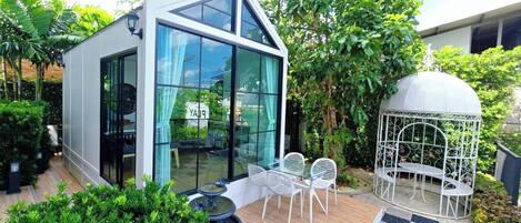 A modern building with large glass windows, a patio with white chairs, and a decorative birdcage.