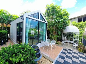Un edificio moderno con amplios ventanales, un patio con sillas blancas y una jaula decorativa.