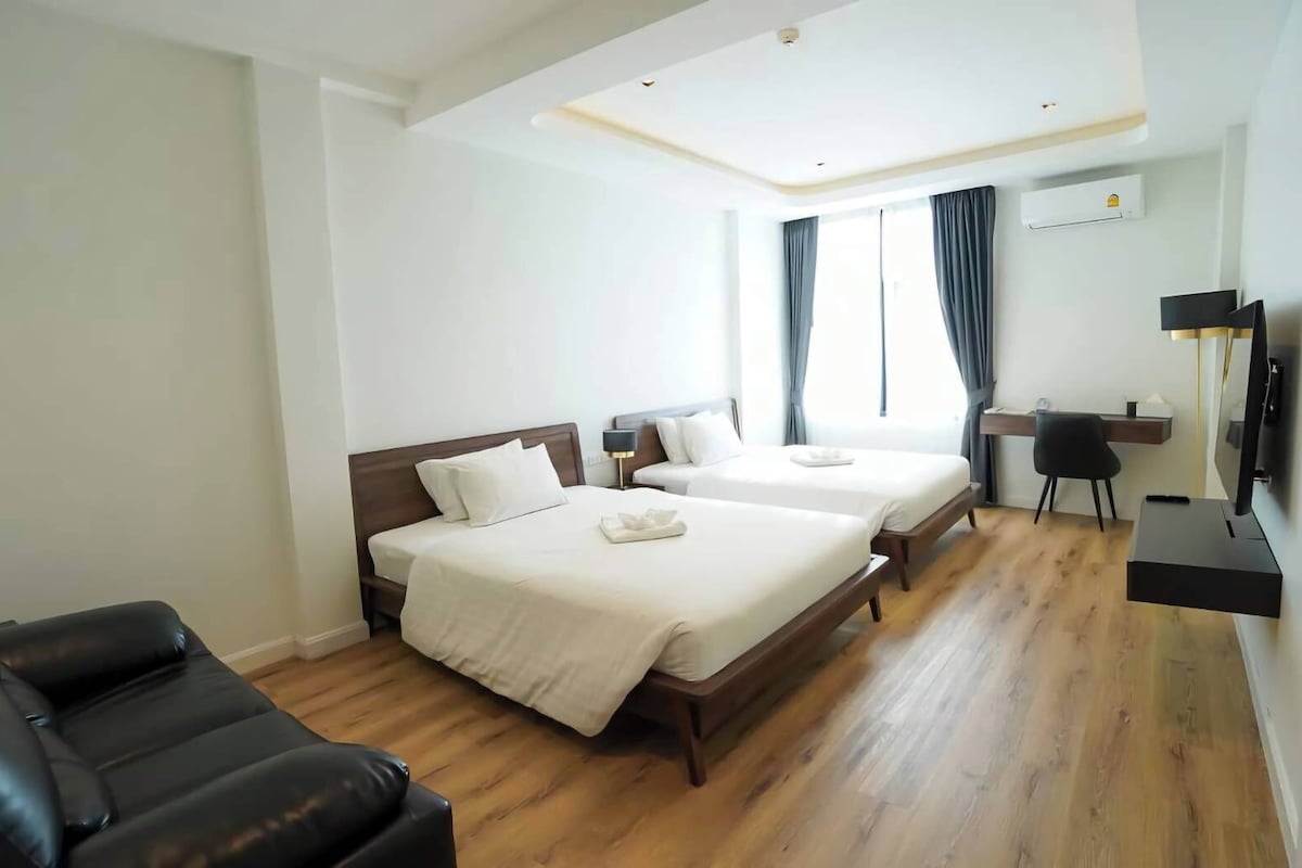 A hotel room with two beds, a desk, a chair, and a TV.
