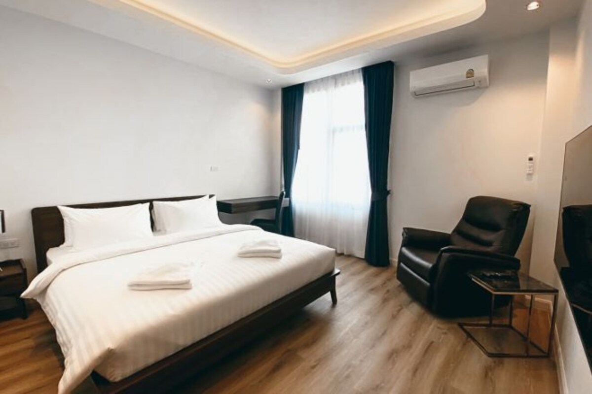 A modern hotel room with a large bed, a leather armchair, a small table, and a TV.