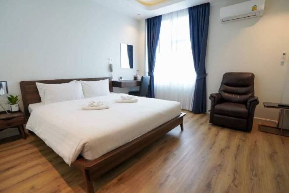 A hotel room with a large bed, a chair, a desk, and a window with curtains.